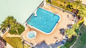 En rektangulär swimmingpool omgiven av en terrass, med solstolar och ett bubbelbad.