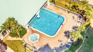 Ein rechteckiger Swimmingpool, umgeben von einer Terrasse, mit Liegestühlen und einem Whirlpool.