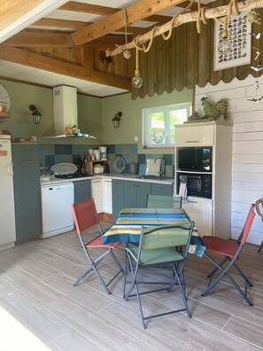 A compact kitchen with a dining area, wooden ceiling beams, and a window. - Typical single-storey Médoc house with outbuildings and swimming pool (Carcans)