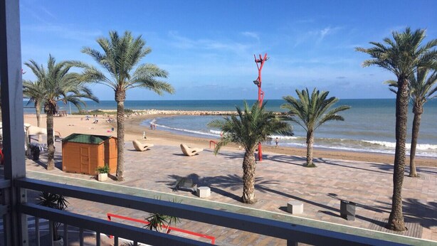Vista sulla spiaggia dal balcone, con palme, una struttura in legno e cielo sereno.