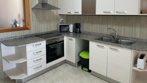 Cucina moderna con mobili bianchi, un forno a microonde, un forno, un lavello e uno sgabello verde.