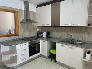 Eine moderne Küche mit weißen Schränken, einer Mikrowelle, einem Backofen, einem Spülbecken und einem grünen Hocker.