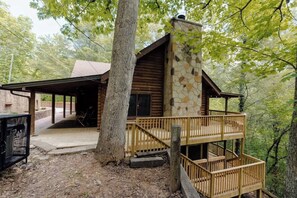 A cabin with a stone exterior, wooden deck, and a covered porch. - Private Cabin in Gatlinburg | Hot Tub + Games + Fire Pit + Scenic Decks (Gatlinburg)