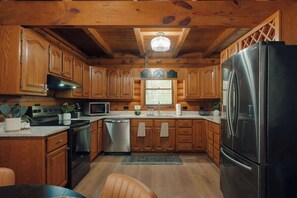A wooden cabin interior with a kitchen featuring wooden cabinets, a stainless steel refrigerator, a microwave, and a sink. - Private Cabin in Gatlinburg | Hot Tub + Games + Fire Pit + Scenic Decks (Gatlinburg)