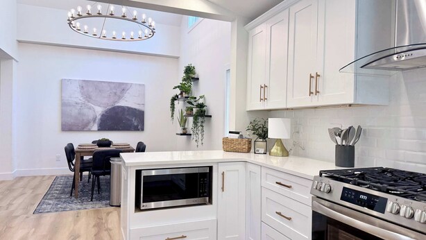 Une cuisine moderne avec des meubles blancs, un four encastré, une cuisinière à gaz et un coin repas comprenant une table et des chaises.