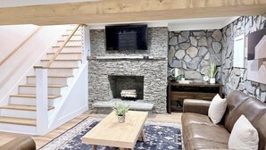 Un salon doté d’une cheminée en pierre, d’un escalier en bois, d’un canapé en cuir et d’un téléviseur à écran plat fixé au-dessus de la cheminée.