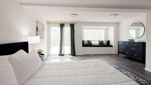 Un dormitorio con cama, cómoda, ventana con cortinas y vista al exterior.