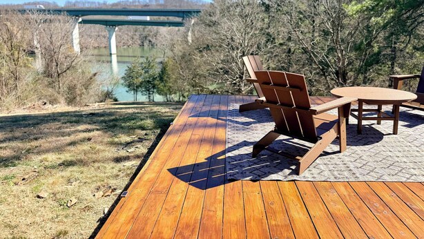 Terraza de madera con mobiliario exterior, vista de un puente y un río.