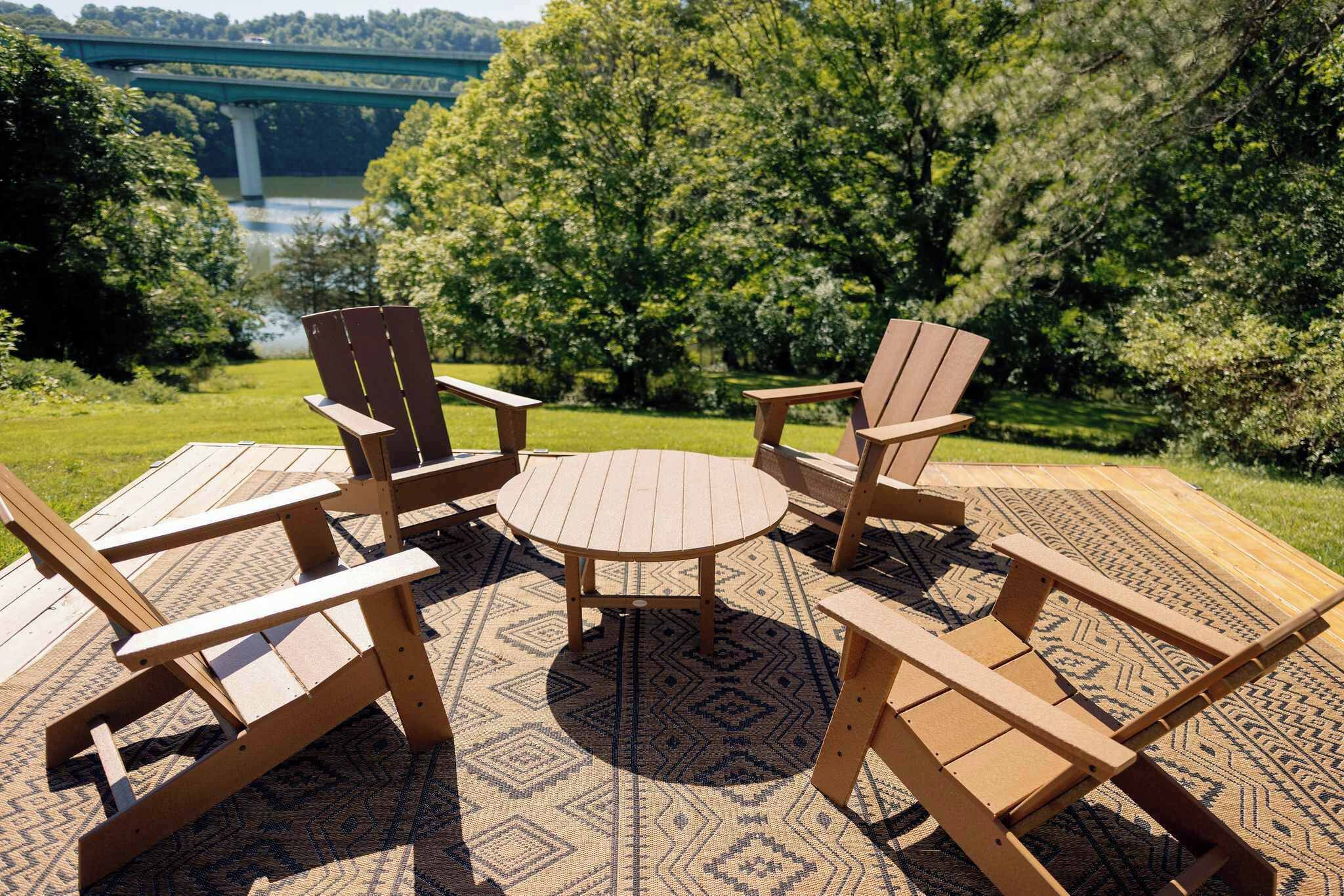 A deck with Adirondack chairs and a round table, overlooking a river and greenery.