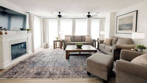Una sala de estar con chimenea, un conjunto de sofás, una mesa de centro y un ventilador de techo.