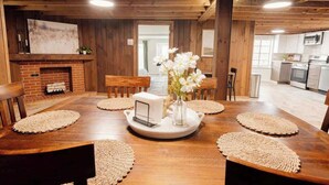 Una mesa de madera para comer con posavasos, un florero con flores y una chimenea.