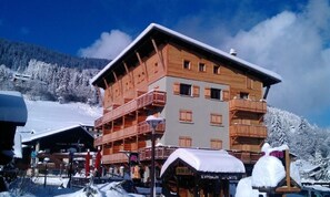 A multi-story wooden building with balconies, a ski slope in the background, and a sign for 'EVASION SPORTS'. - 300m from resort center, 1st floor, parking, tv, ski locker, 40m², Les Gets (Les Gets)