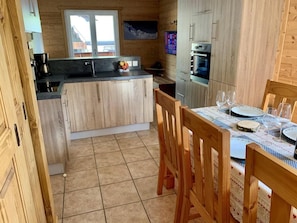 A compact kitchen with wooden cabinets, a central island, a dining table set with plates and glasses, and a window with a view. - 300m from resort center, 1st floor, parking, tv, ski locker, 40m², Les Gets (Les Gets)