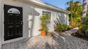 Une maison avec une porte noire, le numéro « 1015 » sur le mur et un pot de fleurs devant.