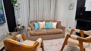 Ein Wohnzimmer mit einer Couch, zwei Holzstühlen, einem Teppich und einem Fernseher.