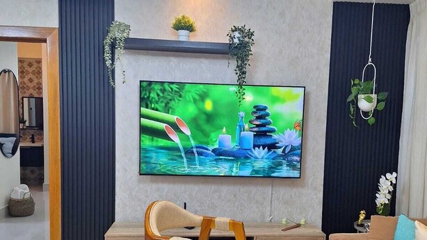 Ein modernes Wohnzimmer mit Fernseher, Holzstühlen, einer Couch und einer Deckenleuchte.