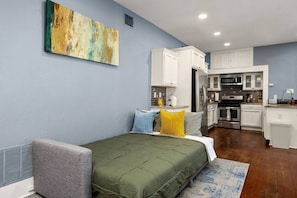 A bedroom with a bed, a bedside table, a nightstand, a window, and a kitchen area with cabinets and appliances. - Family-friendly Stay A Happy Getaway! (San Antonio)