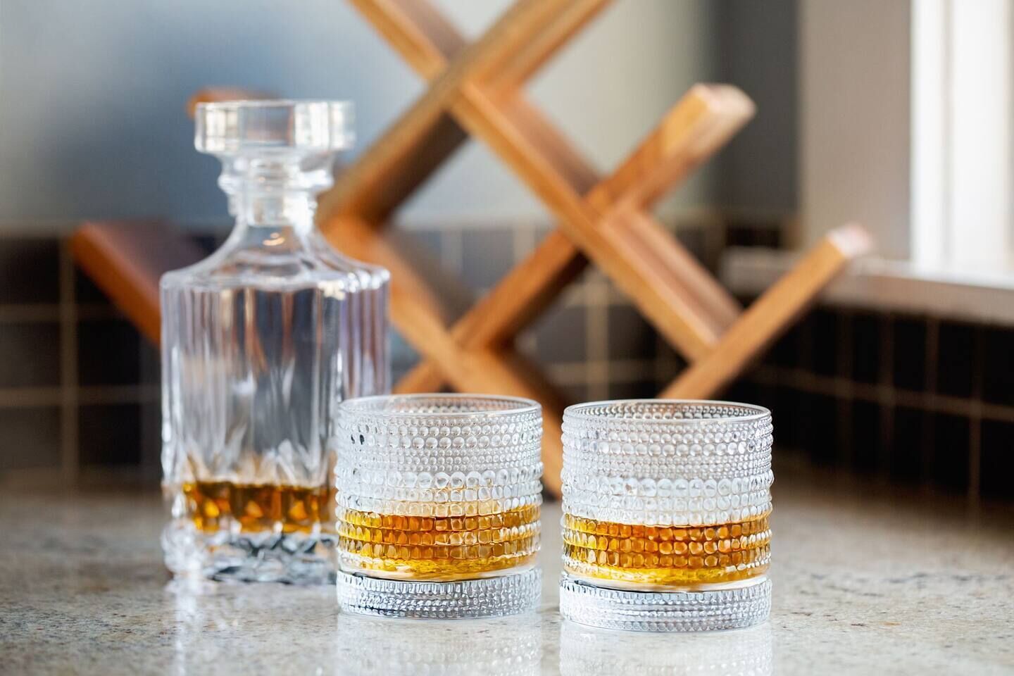 Een glazen karaf en twee glaasjes met een reliëfpatroon, geplaatst op een reflecterend oppervlak.