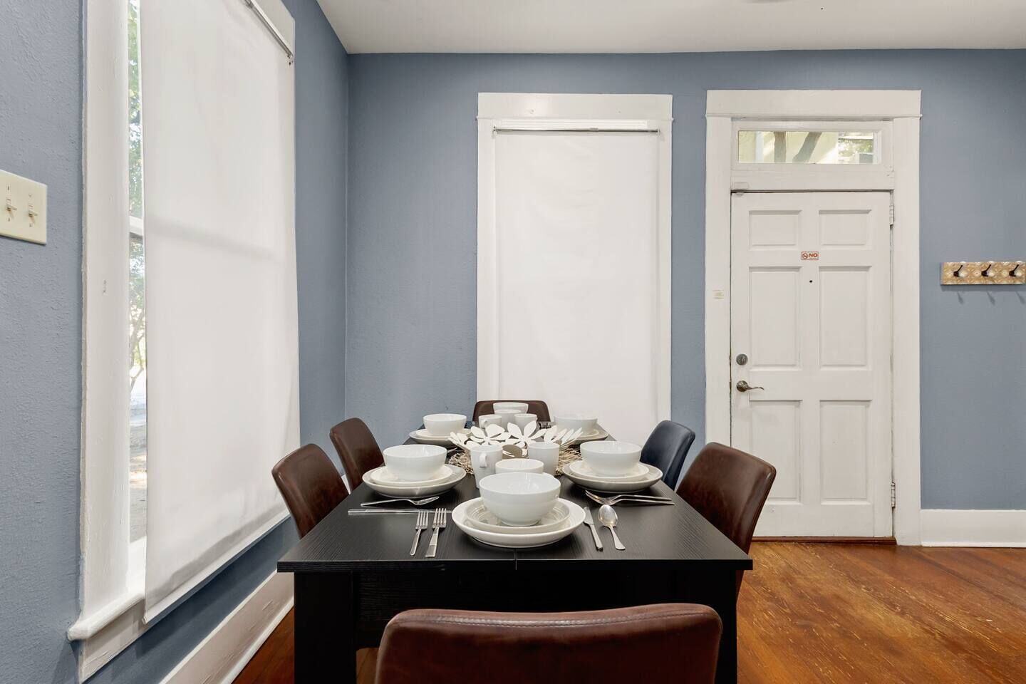 Comedor con una mesa de madera oscura dispuesta para seis, platos, cuencos y cubiertos blancos.