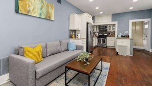 Una sala de estar moderna con un sofá gris, una mesa de centro y una cocina al fondo.