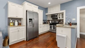 Una cocina con armarios blancos, electrodomésticos de acero inoxidable y piso de madera.
