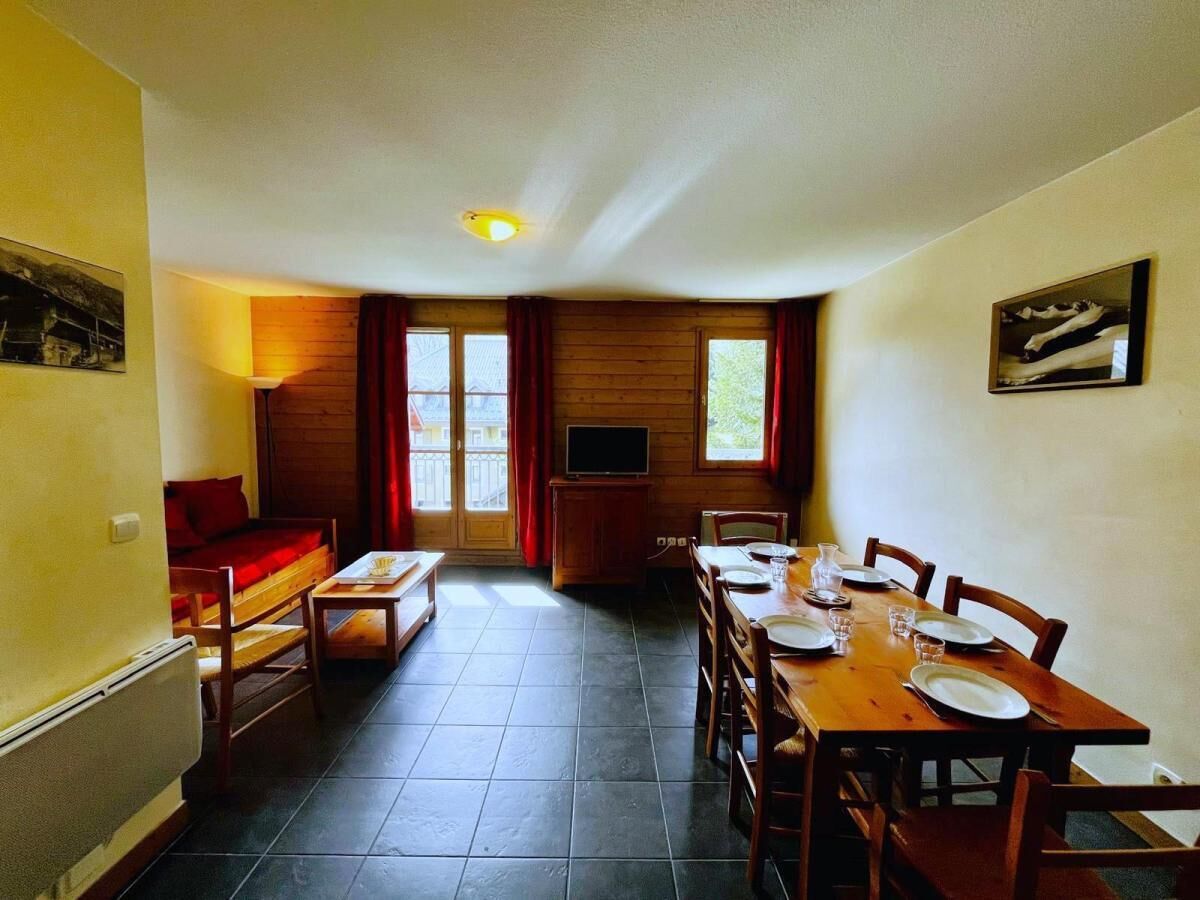 A dining area with a table set for four, a sofa, a TV, and a window with curtains.