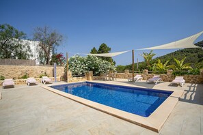 Ein rechteckiger Pool mit einer gefliesten Kante, umgeben von Steinplatten und weißen Liegestühlen.