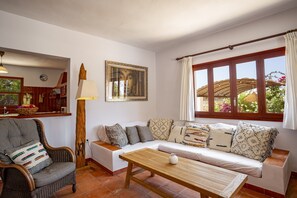 Ein Wohnzimmer mit einer Couch, einem Sessel, einem Holztisch, einer Lampe, einem Gemälde und einem Fenster mit Vorhängen.