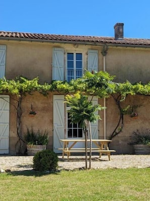 A building with a tiled roof, a wooden bench, and potted plants. - Gîte Bambou - Country charm and heated swimming pool in the heart of Charente (Chadurie)