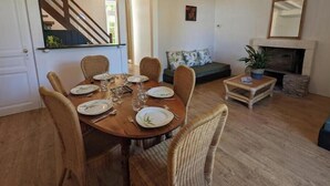 A dining area with a wooden table and wicker chairs, a staircase, a sofa, a fireplace, and a mirror. - Gîte Bambou - Country charm and heated swimming pool in the heart of Charente (Chadurie)