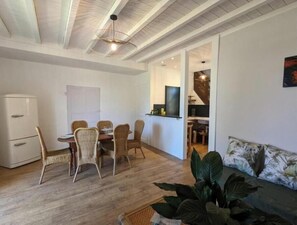 A dining area with a table and chairs, a kitchenette, a sofa, and a plant. - Gîte Bambou - Country charm and heated swimming pool in the heart of Charente (Chadurie)