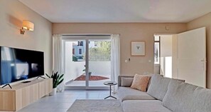 Ein modernes Wohnzimmer mit Flachbildfernseher, einer Couch, einem kleinen Tisch und einer Schiebetür zu einem Außenbereich.