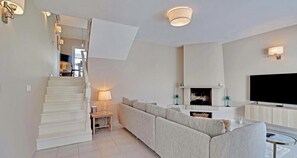 Ein modernes Wohnzimmer mit Treppe, Sofa, Fernseher und Kamin.