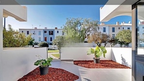Ein moderner Balkon mit Topfpflanzen, freiem Blick auf angrenzende Gebäude und einem Fliesenboden.
