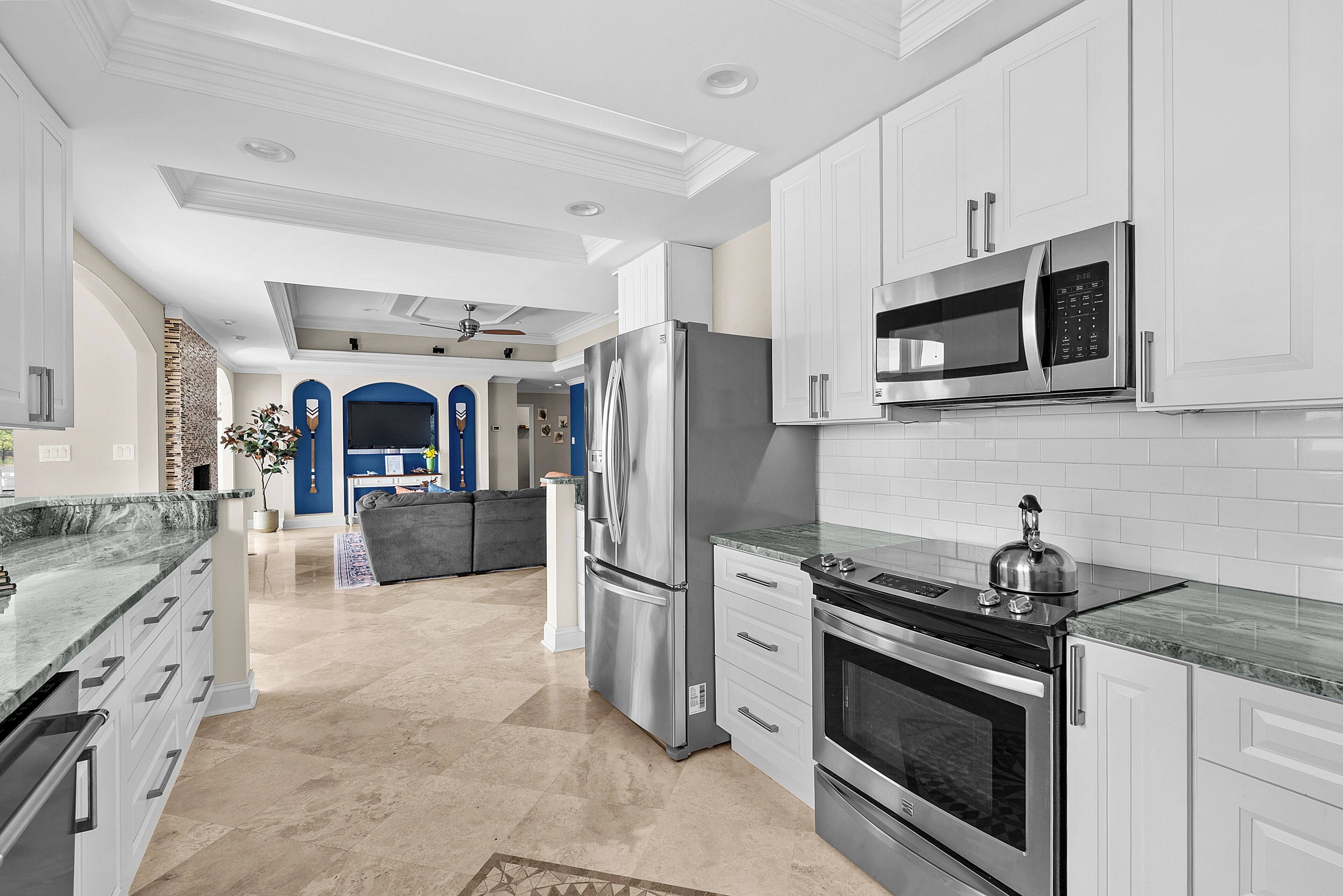 A modern kitchen with stainless steel appliances, white cabinetry, and a marble countertop.