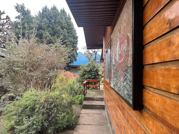 Un edificio de madera con un porche cubierto, un sendero de piedra y abundante vegetación.