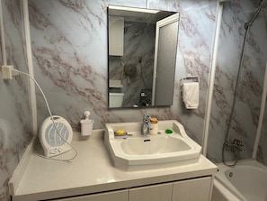 Baño con pared de mármol, lavamanos con espejo, ducha de mano y secador de pelo enchufado.