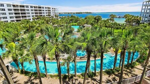 A resort with multiple swimming pools surrounded by palm trees, a view of the ocean, and a large hotel building. - Destin West Bayside Sandpiper #505 (Fort Walton Beach)