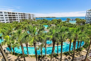 Ein Resort mit mehreren Schwimmbecken, umgeben von Palmen, mit Blick auf den Ozean und einem großen Hotelgebäude.