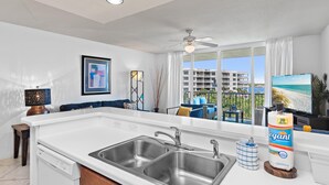A modern kitchen with a large island, stainless steel sinks, and a view of a balcony with outdoor furniture. - Destin West Bayside Sandpiper #505 (Fort Walton Beach)