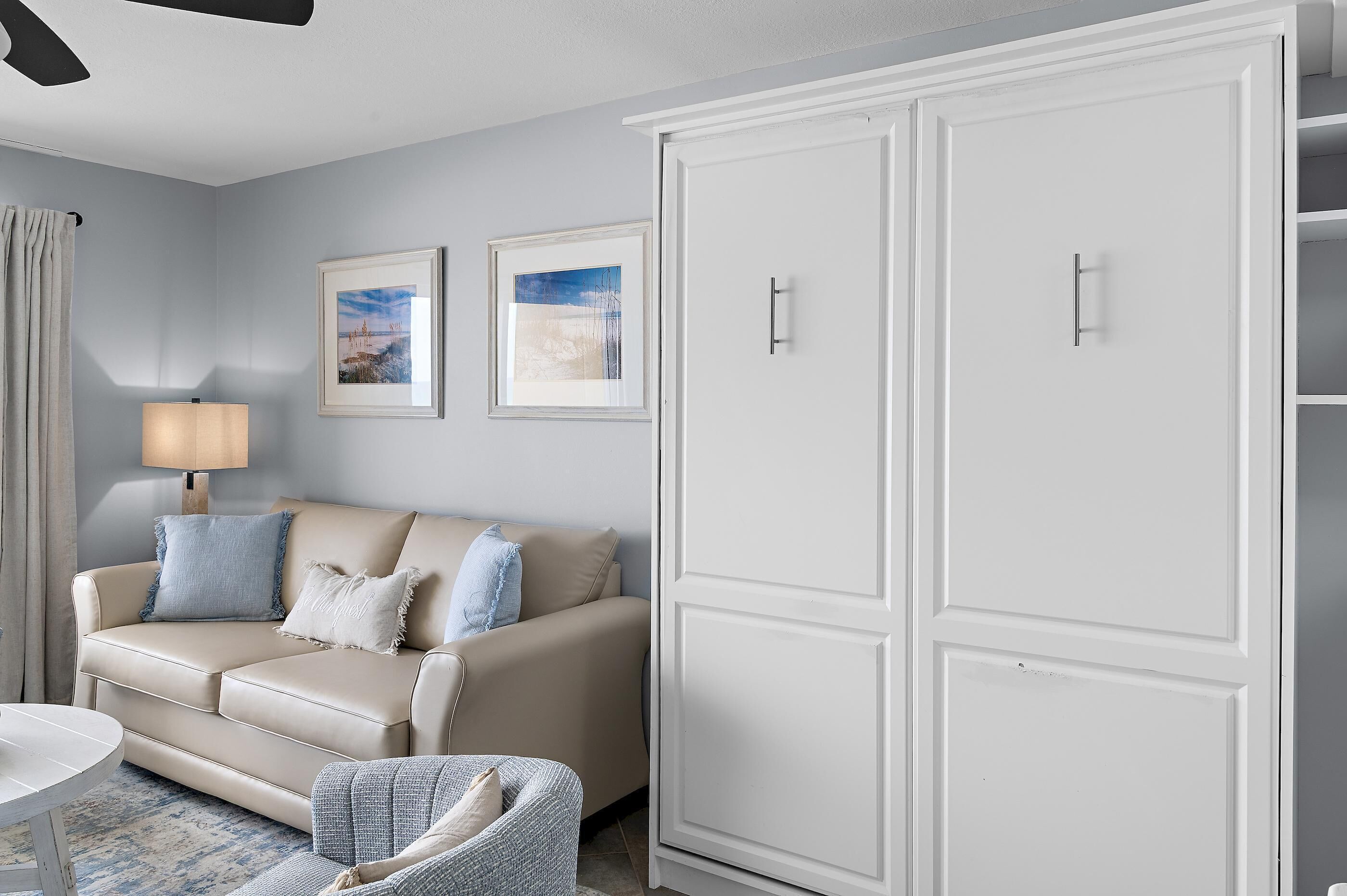 A room with a beige sofa, a white wardrobe, and two framed pictures on the wall.