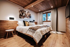 Ein Schlafzimmer mit einem Holz-Kopfteil, einem großen Bett mit weißer und brauner Decke, einem kleinen runden Tisch und einem Bärenbild an der Wand.