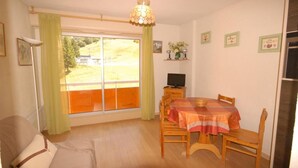 Ein Zimmer mit Esstisch, Stühlen, einer Couch, einem Fernseher und einem Fenster mit Vorhängen.