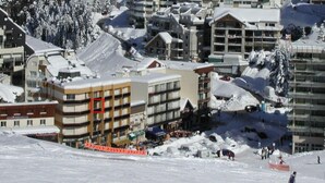 Ein schneebedecktes Skigebiet mit mehrstöckigen Gebäuden, einer Seilbahn und einer Skipiste.
