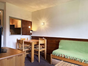 Ein Zimmer mit einem Holztisch, Stühlen, einem grünen Sofa, einem Holzschrank und einer Wandleuchte.