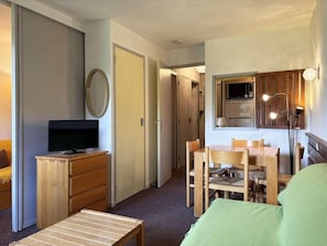 Ein kompaktes Hotelzimmer mit Fernseher, Holzmöbeln, einem Esstisch und einer Küchenzeile.
