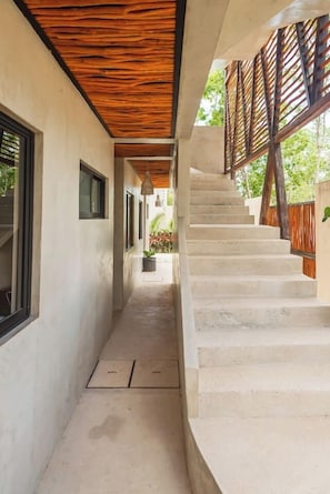 A narrow corridor with a wooden ceiling, a concrete staircase, and a view of greenery outside. - NEW Apartment AREIA Tulum 1BR Style/Comfort (Tulum)