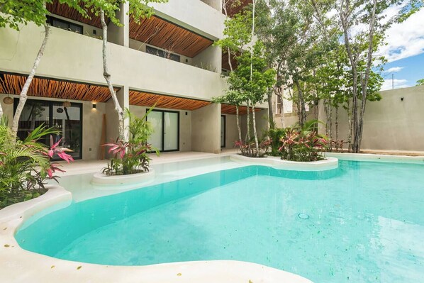 A modern building with a swimming pool, surrounded by tropical plants and trees. - NEW Apartment AREIA Tulum 1BR Style/Comfort (Tulum)