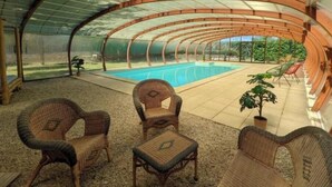 A covered outdoor area with a pool, wicker furniture, and a view of greenery.