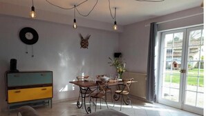 A dining area with a table and chairs, a sofa, a clock, and a radiator.